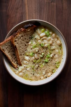 a white bowl filled with soup and two pieces of bread on top of a wooden table