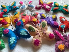 many different colored felted butterflies on a white tablecloth with pins attached to them