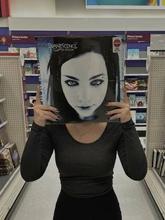 a woman holding up a book in front of her face while standing in a store aisle