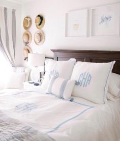 a bed with white and blue pillows in a bedroom next to two pictures on the wall