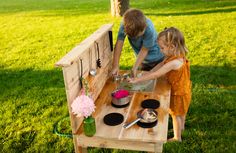 two young children are playing with pots and pans on a wooden bench in the grass