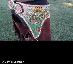 a woman wearing a brown leather belt with flowers and leaves on it, standing in the grass