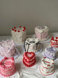 many different types of cakes on display on a white tablecloth with red, pink and blue decorations