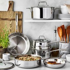 stainless steel pots and pans are lined up on the kitchen counter with wooden utensils