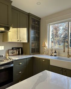 a kitchen with green cabinets and white counter tops, an oven and sink are in front of a large window