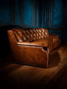 a brown leather couch sitting on top of a wooden floor next to a blue wall