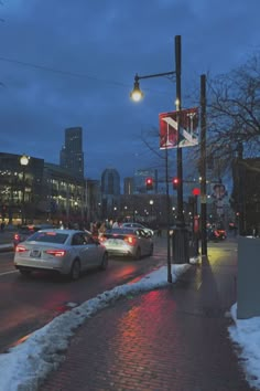 cars are driving down the street at night in the city with snow on the ground