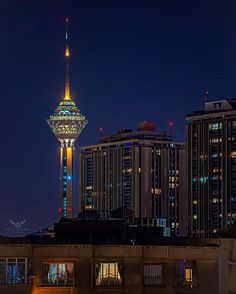 a city skyline at night with tall buildings in the foreground and a brightly lit tower