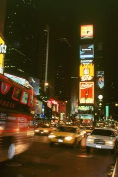 a busy city street at night with cars and neon signs on the side of buildings