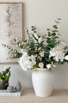 a white vase filled with flowers sitting on top of a wooden table next to plants