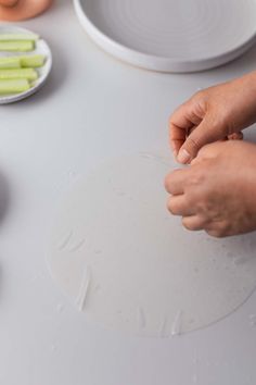 the person is making something on the table with their hands and plates in the background