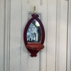 a mirror hanging on the side of a white door with a red shelf below it