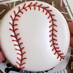 a person is holding a baseball ornament with red stitching on the outside