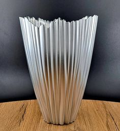 a white vase sitting on top of a wooden table next to a black wall in the background