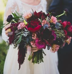 a close up of a person holding a bouquet of flowers and greenery in their hands