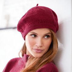 a woman wearing a red hat leaning against a wall