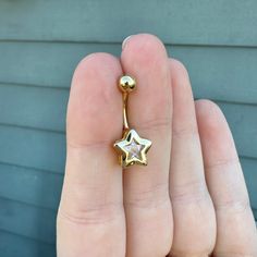 a person's hand holding a gold star shaped nose ring with a diamond in the middle