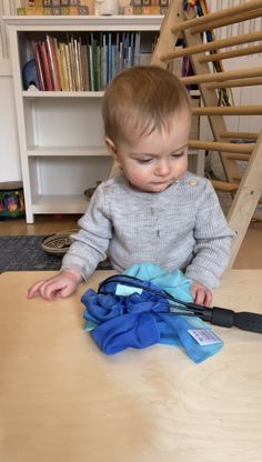 a toddler sitting on the floor playing with a blue bag in front of a bookshelf