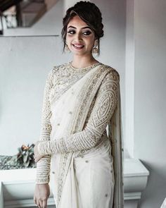 a woman in a white sari and matching jewelry poses for the camera with her hands on her hips