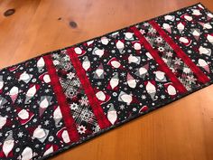 a black table runner with red and white snowmen on it, sitting on a wooden floor