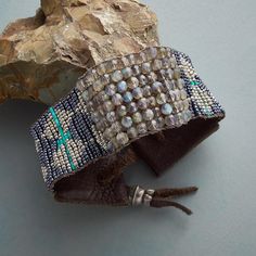 a leather bracelet with beads and stones on top of a rock next to a piece of driftwood