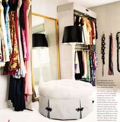 a room with clothes hanging on the wall and a round ottoman in front of a mirror