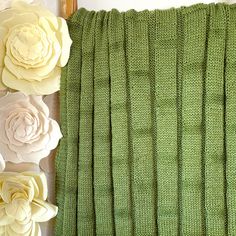 green knitted blanket with flowers on top and two white roses in the middle next to it