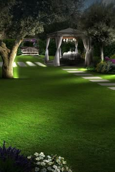 a gazebo in the middle of a lush green park at night with flowers and trees