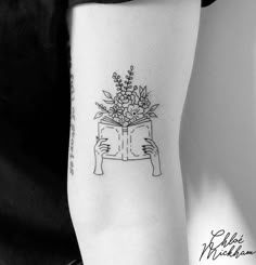 a woman's arm with a book and flowers on it