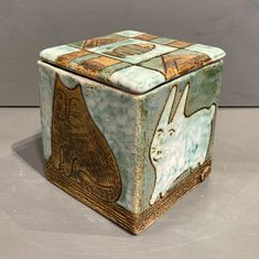 a ceramic box with an image of a rabbit and a cat on the inside, sitting on a table