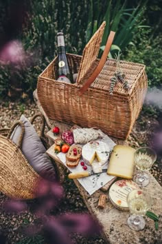 a picnic basket with cheese, bread and wine on it next to a bottle of wine