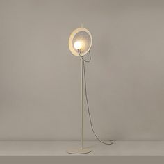 a white floor lamp with a round light bulb on the base and a wire running through it