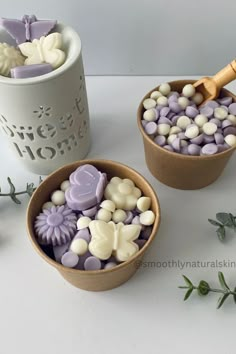 two bowls filled with purple and white candies next to a cup full of flowers