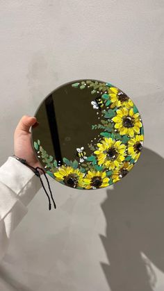 a hand holding a mirror with sunflowers painted on it