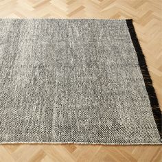 a black and white rug with fringes on top of wood flooring in an empty room