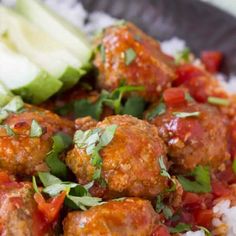 meatballs and rice with garnishes on a black plate, ready to be eaten