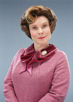 a woman with short hair wearing a pink sweater and red bow tie, standing in front of a gray background