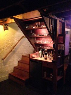 a bar with shelves filled with liquor bottles and glasses next to a stair case in a dimly lit room