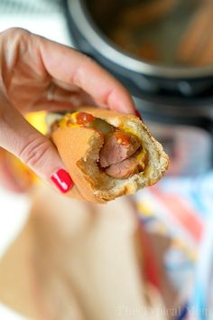 a person holding a hot dog with mustard and ketchup in their left hand