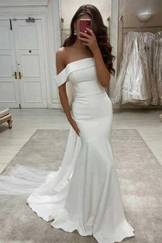 a woman in a white dress taking a selfie with her cell phone while wearing an off the shoulder wedding dress