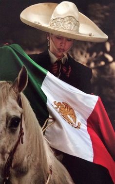 a man riding on the back of a white horse holding a mexican flag in his hand