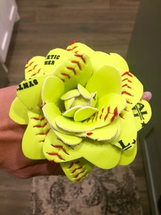 a person holding a yellow flower made out of baseballs