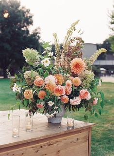 an arrangement of flowers is sitting on a wooden table with candles and vases next to it