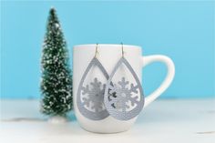 a pair of silver earrings sitting on top of a white cup next to a small christmas tree