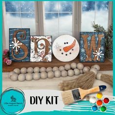 a snowman is sitting next to some wooden letters and paintbrushes on a table