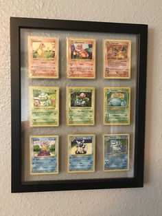 a collection of pokemon trading cards mounted in a shadow box with black frame on the wall