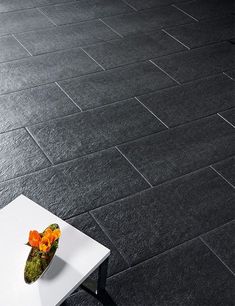 a white table topped with a vase filled with flowers on top of a black tiled floor