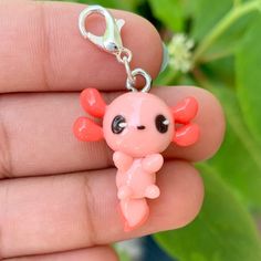 a little pink doll with big eyes sitting on a keychain in someone's hand