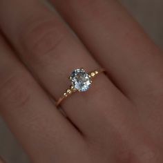 a woman's hand with a yellow gold ring and an aquamarine blue diamond