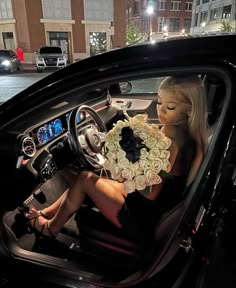 a woman sitting in the driver's seat of a car holding a bouquet of flowers